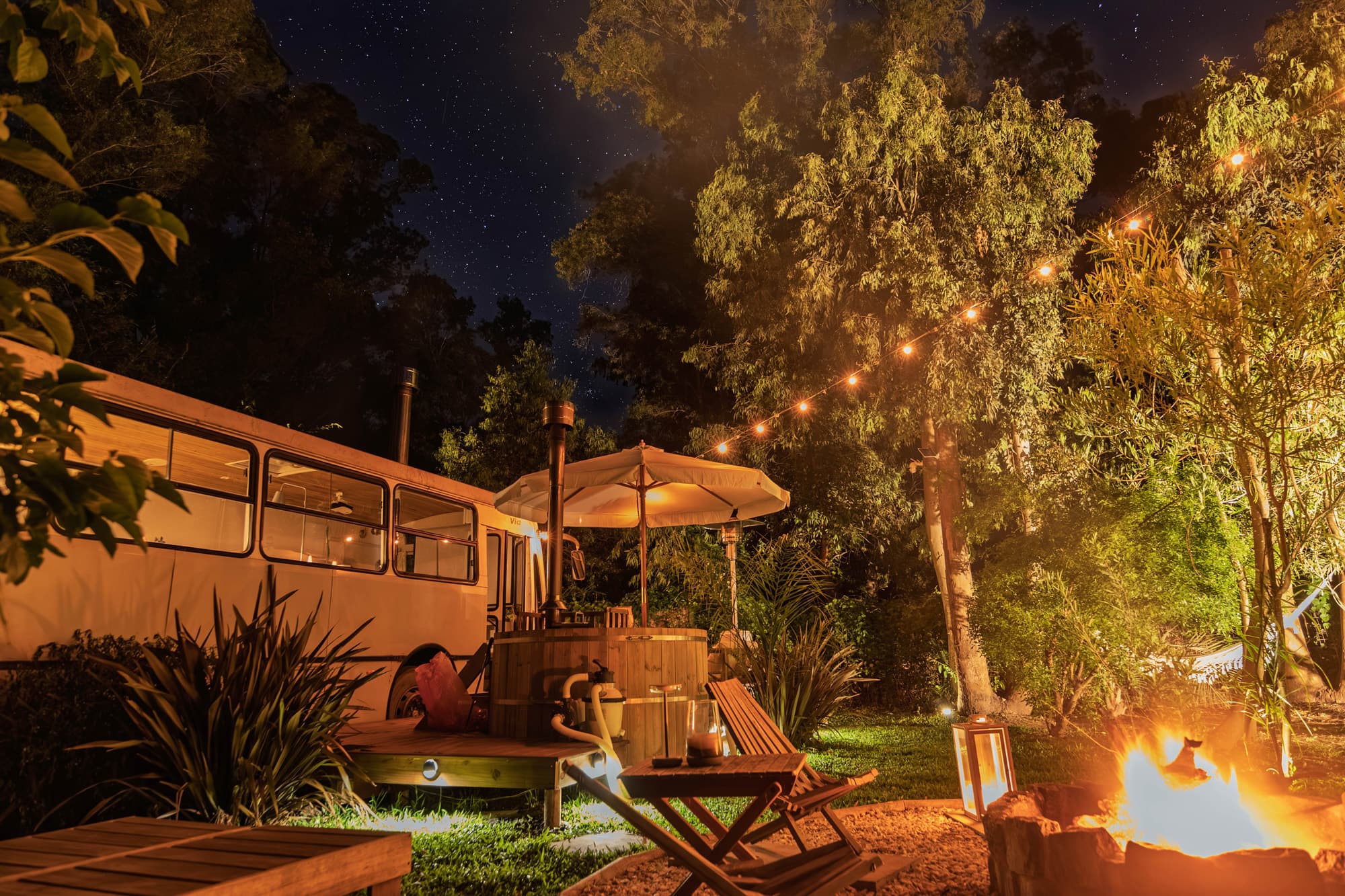 BondiHouse de noche — fogón encendido y tina de madera bajo el cielo estrellado de Uruguay