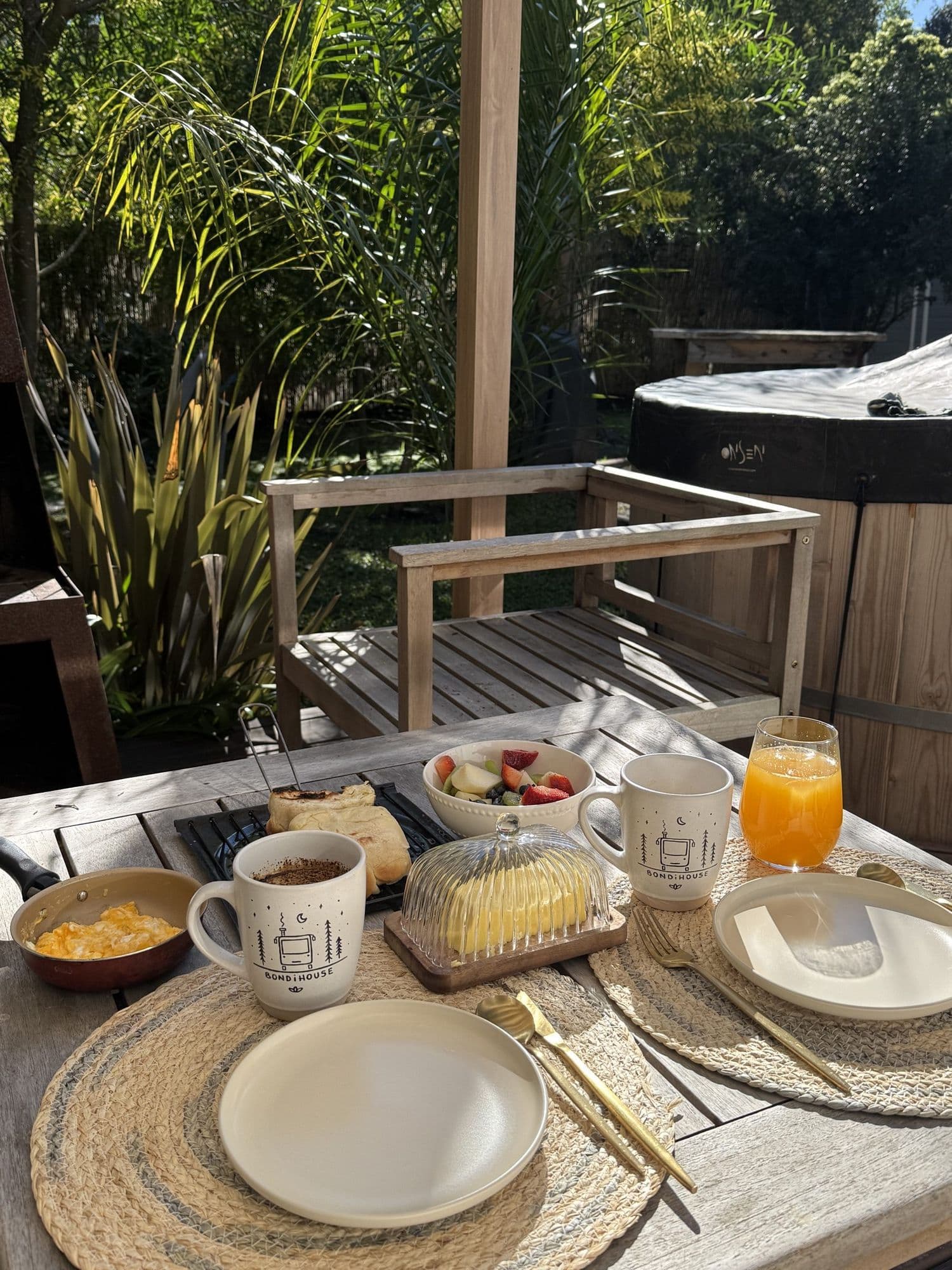 Desayuno servido al aire libre en el deck de BondiHouse, con la tina tapada al fondo