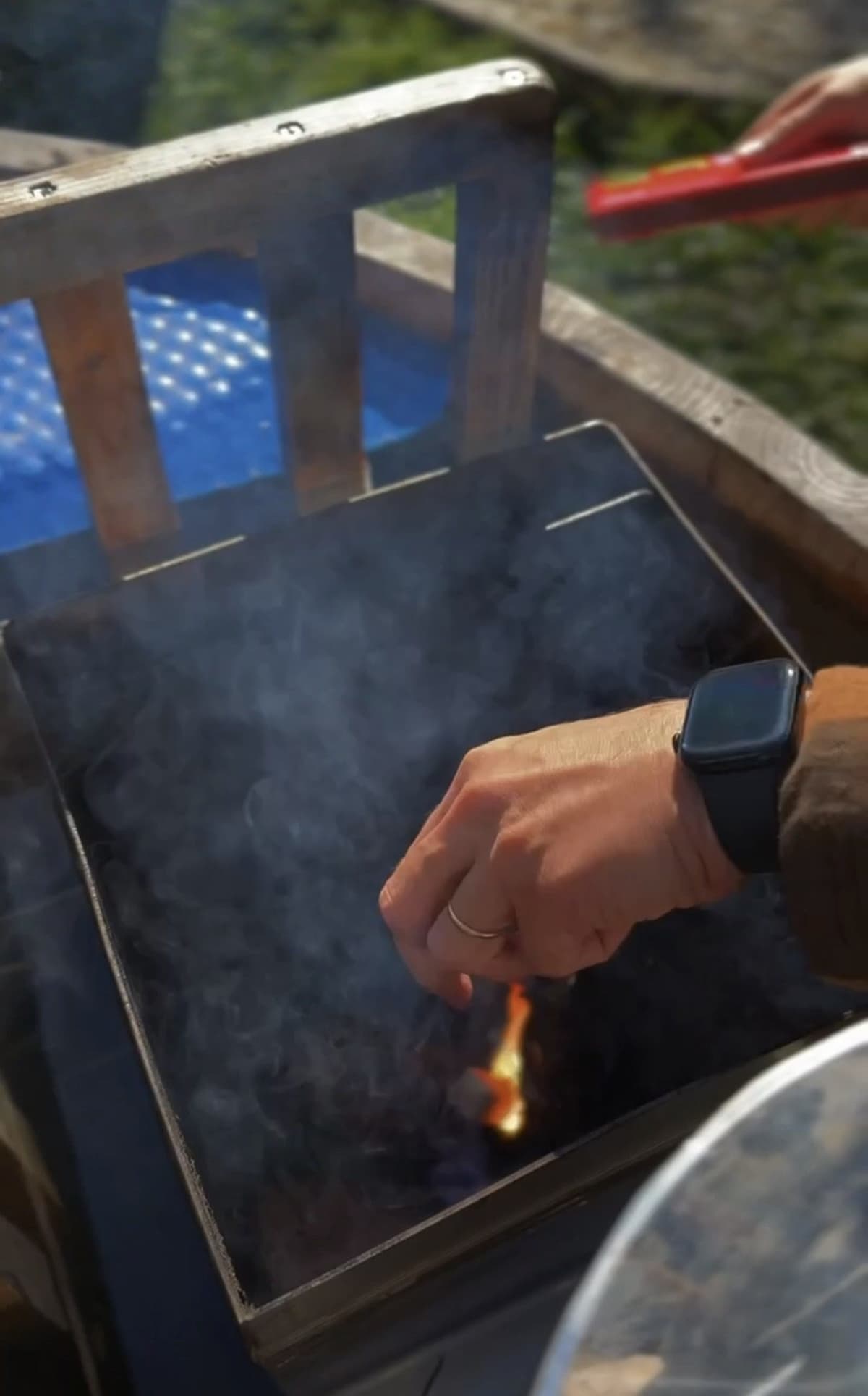 Una mano prendiendo el fuego dentro de la caldera de la tina, con la tapa abierta y humo