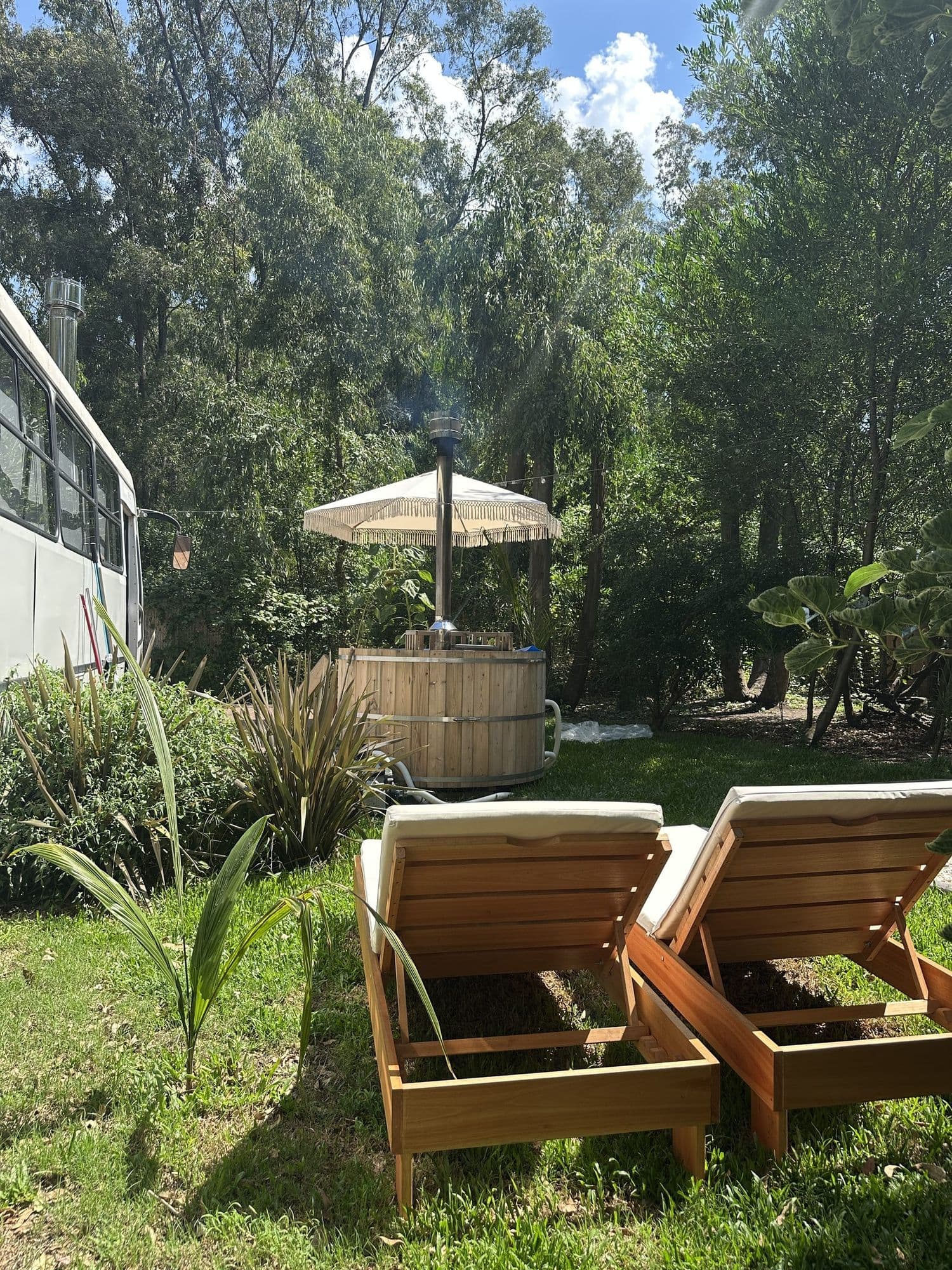Dos reposeras de madera en el jardín de BondiHouse, con la tina y la sombrilla al fondo