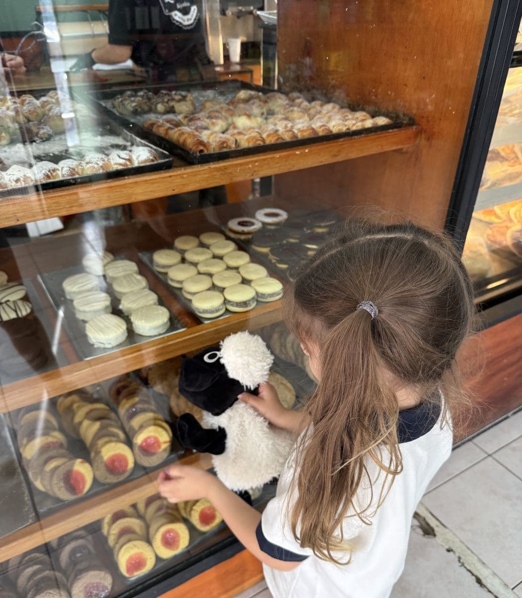 Franca, con su oveja de peluche, mirando la vitrina de la Panadería La Loma llena de alfajores, masitas y medialunas