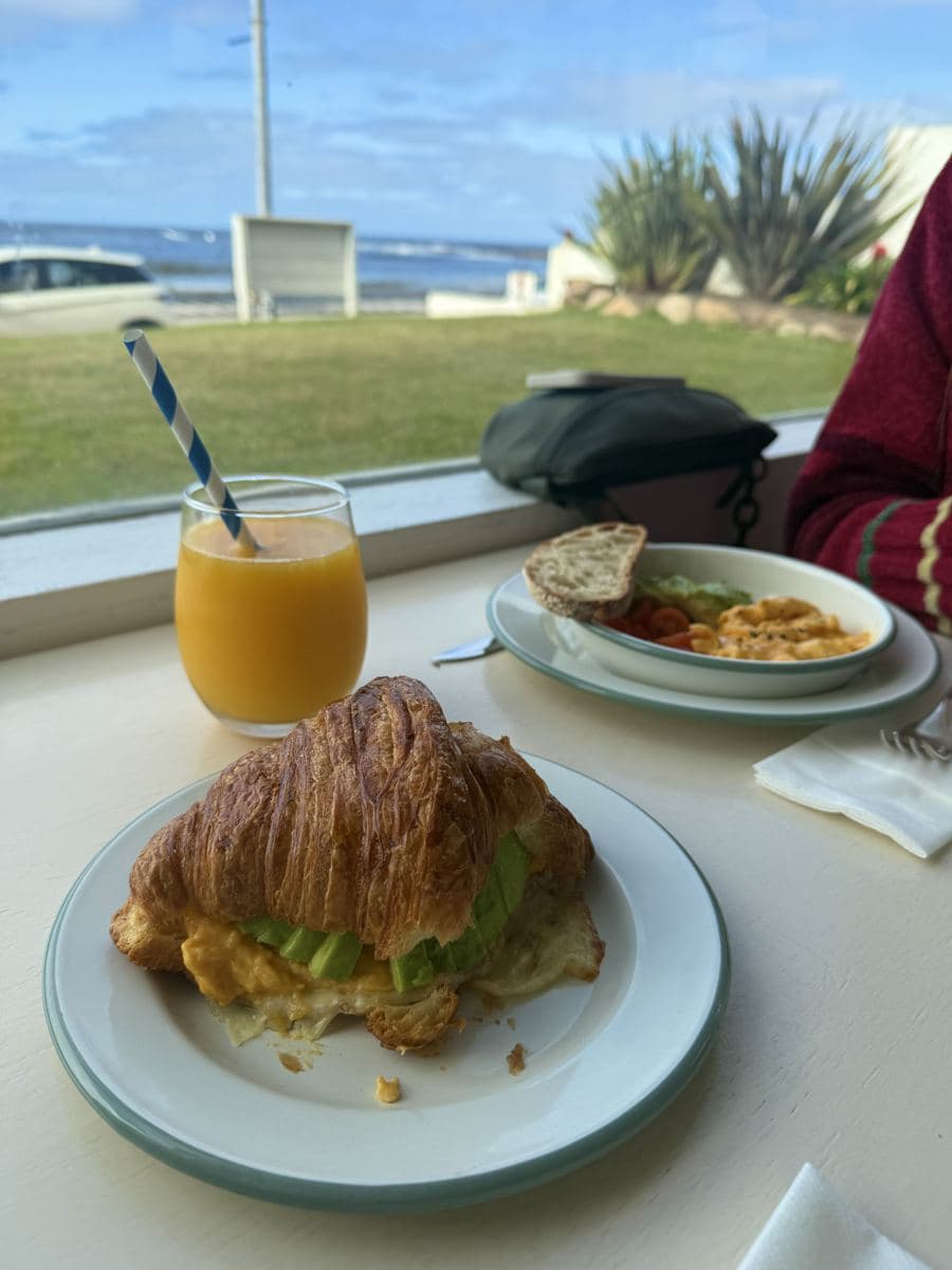 Desayuno en Vitaminas frente a la Brava: medialuna con huevos revueltos y palta, jugo de naranja y el mar de fondo