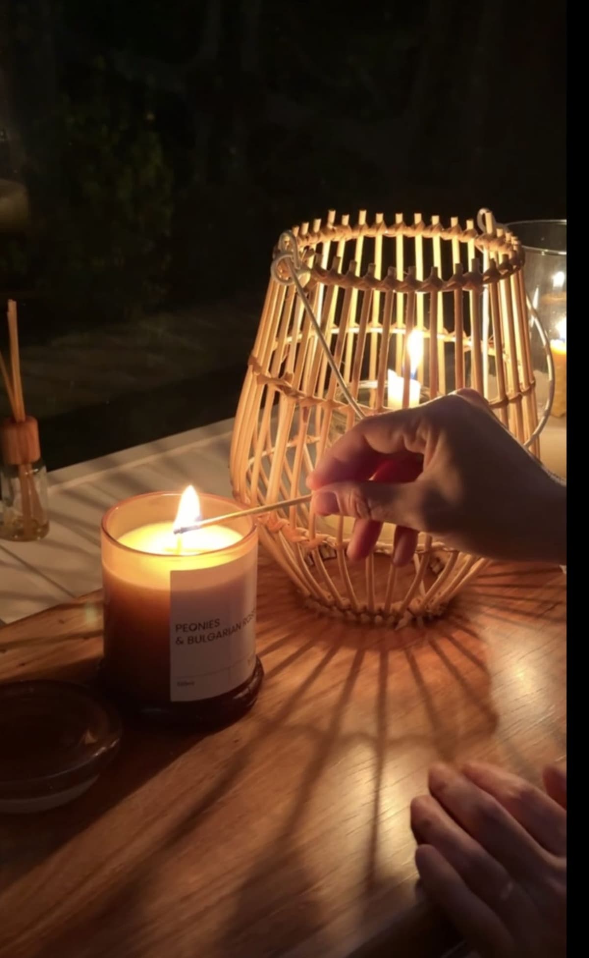 Mano encendiendo una vela junto a un farol de ratán en el Bondi
