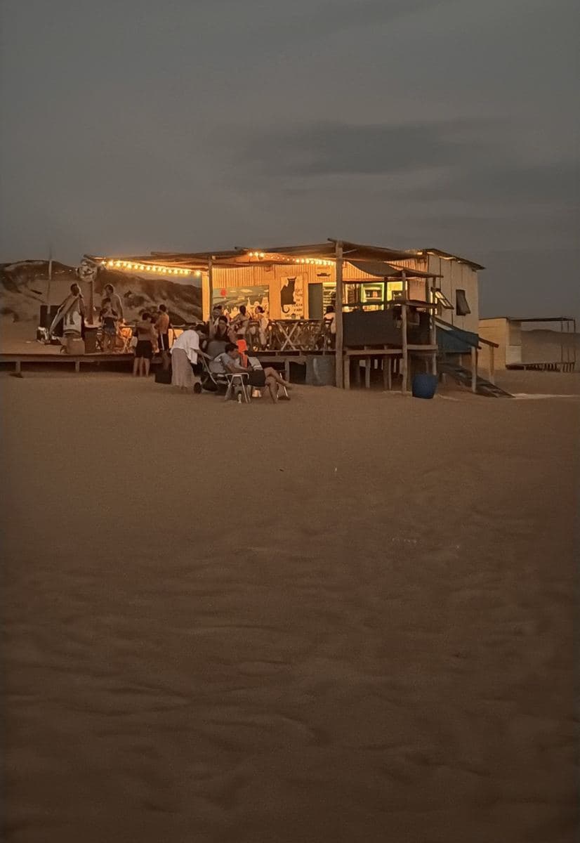 O Chiringuito de Ocean Park ao anoitecer: o quiosque na areia, iluminado com cordões de luzes quentes