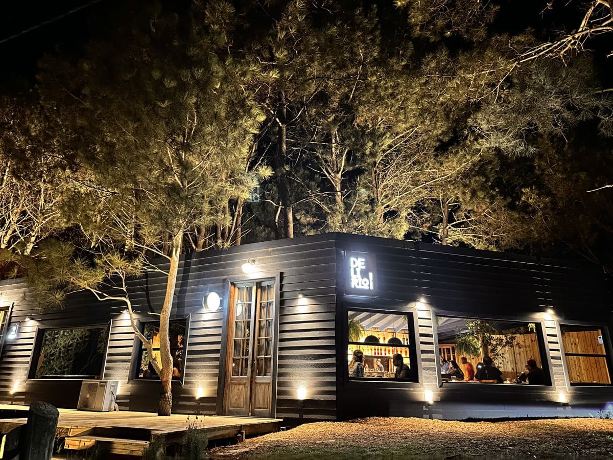 O Delirio à noite: a casa de madeira escura iluminada entre pinheiros, com gente jantando atrás das janelas
